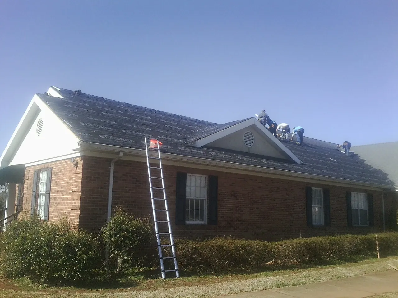 Crew tearing shingles off a brick ranch roof with a ladder set — Metal Roof Repair work by our crew in Bellwood