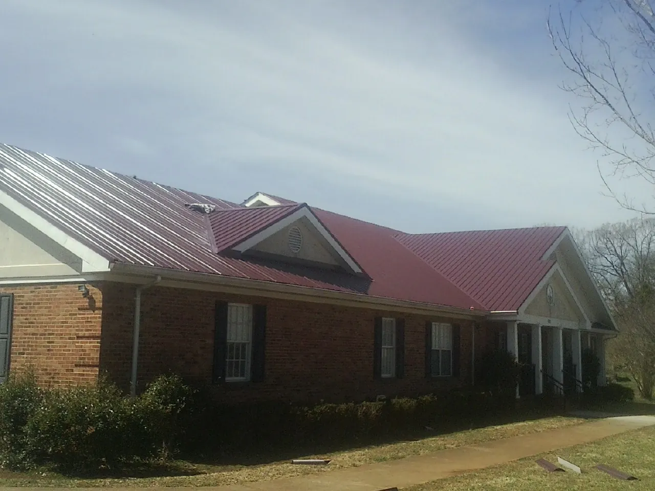 Red metal roof with gabled entries on a long brick building, from a Hail Damage Roof Repair job in Bellwood