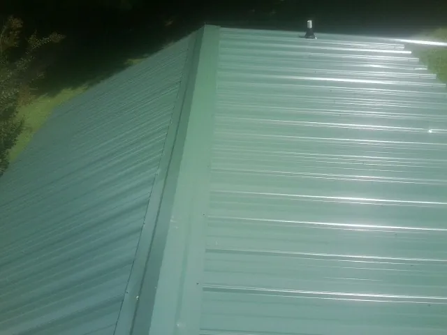 New green metal panels meeting at the ridge of a roof — Flat Roof Repair work by our crew in Bellwood