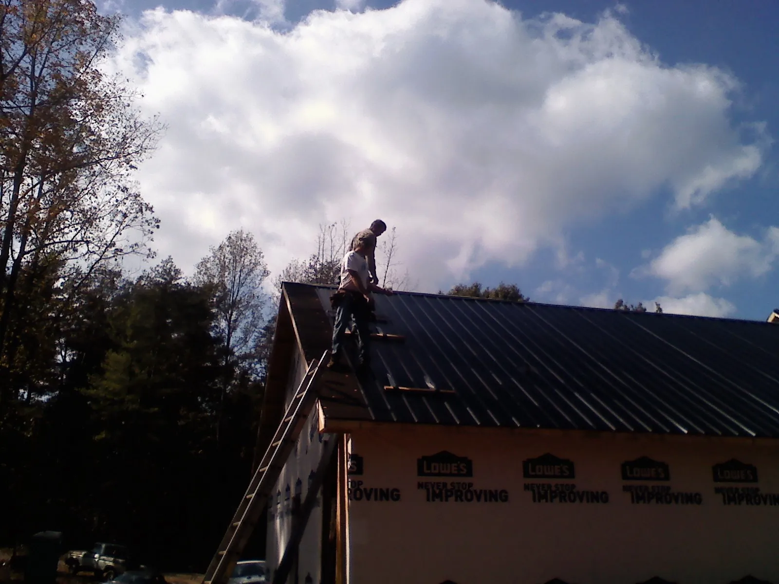 Roofer fastening dark metal panels high against a cloudy sky, from a Roof Inspection job in Bellwood